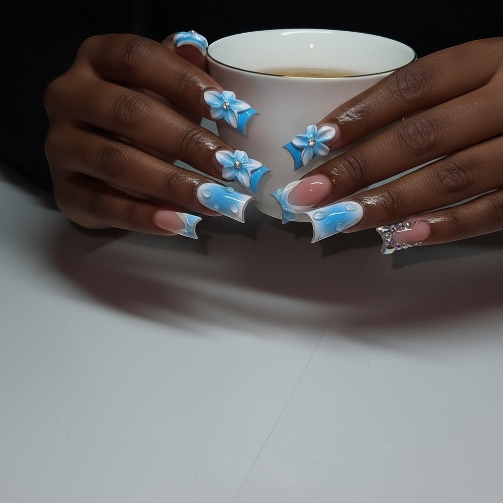 Aurapal press-on nails featuring blue French tips, 3D floral art, and water droplet accents on a person holding a cup.