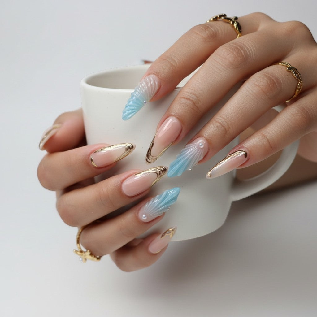AuraPal press-on nails with blue seashell design and gold accents. Almond shape, ombre blue to clear.