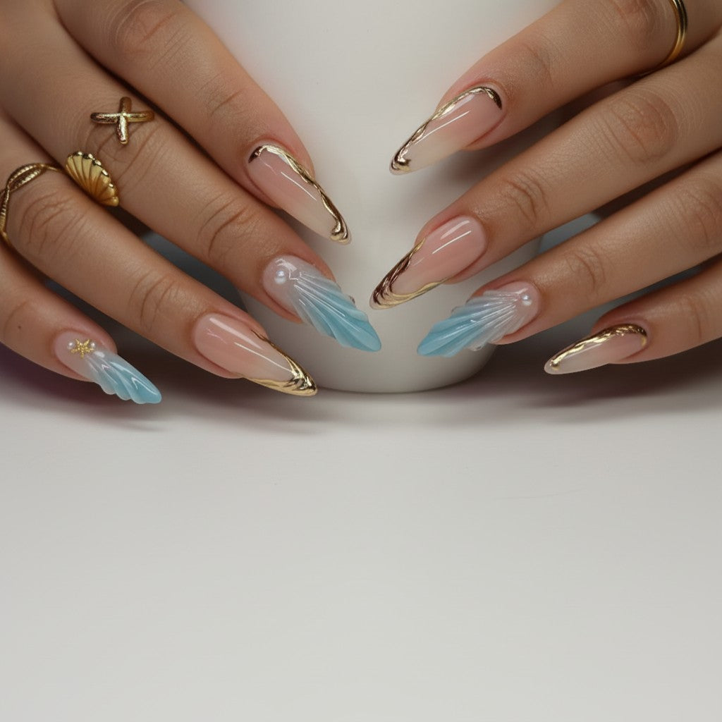 AuraPal press-on nails with blue seashell design and gold accents. Almond shape, ombre blue to clear.