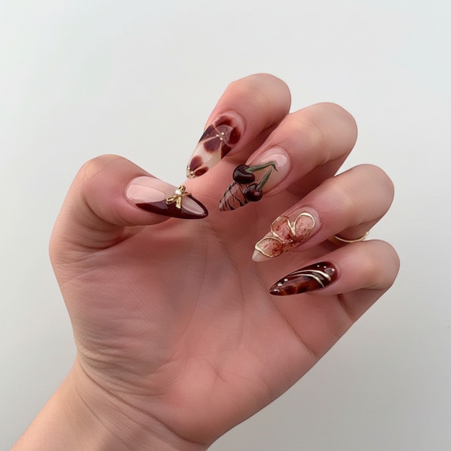 Aurapal Aura23 press-on nails in brown and clear with 3D cherry, bow, and flower charms. Almond shape.
