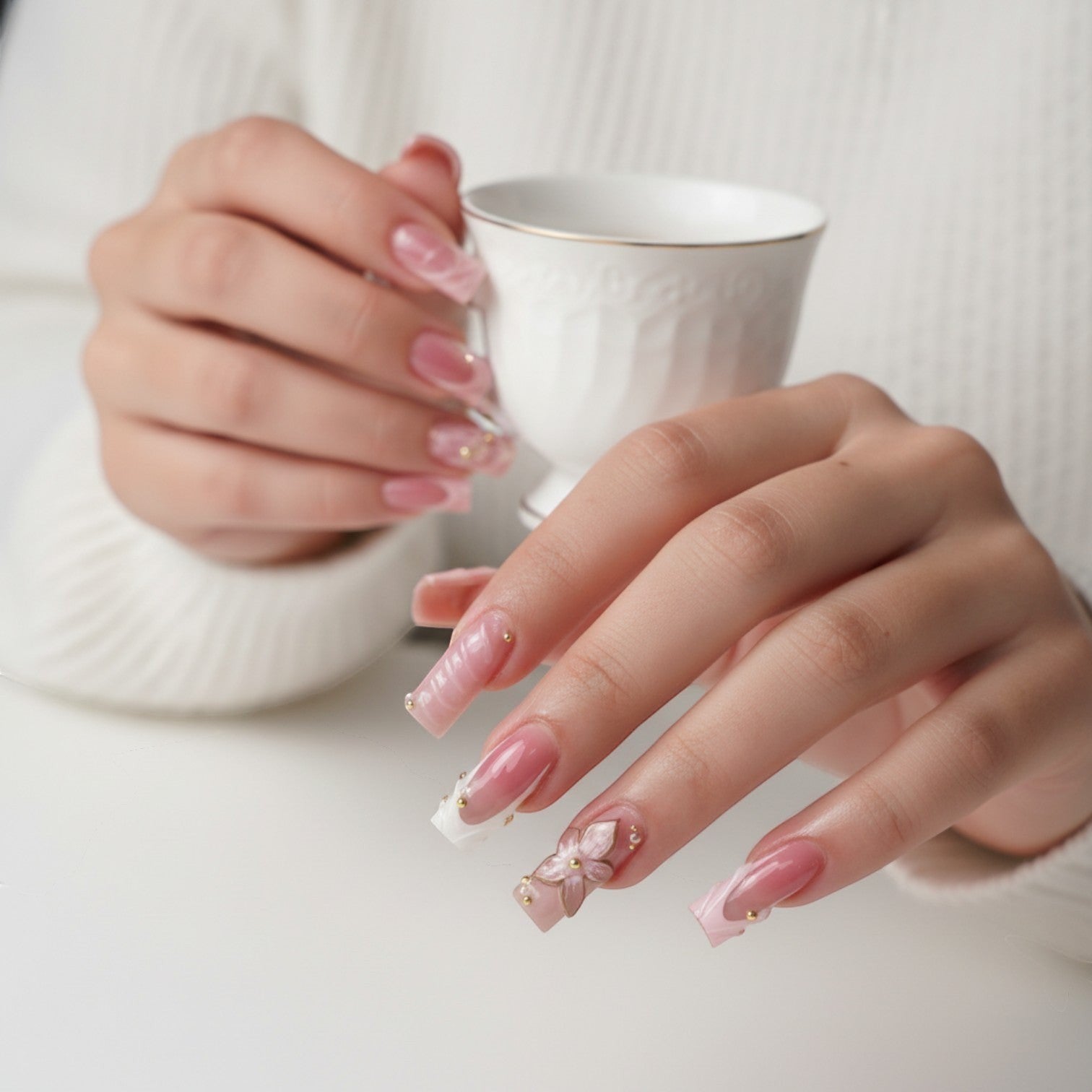Aura50 press-on nails in pink and clear with gold accents and a 3D flower design. Square tips with French manicure detail.