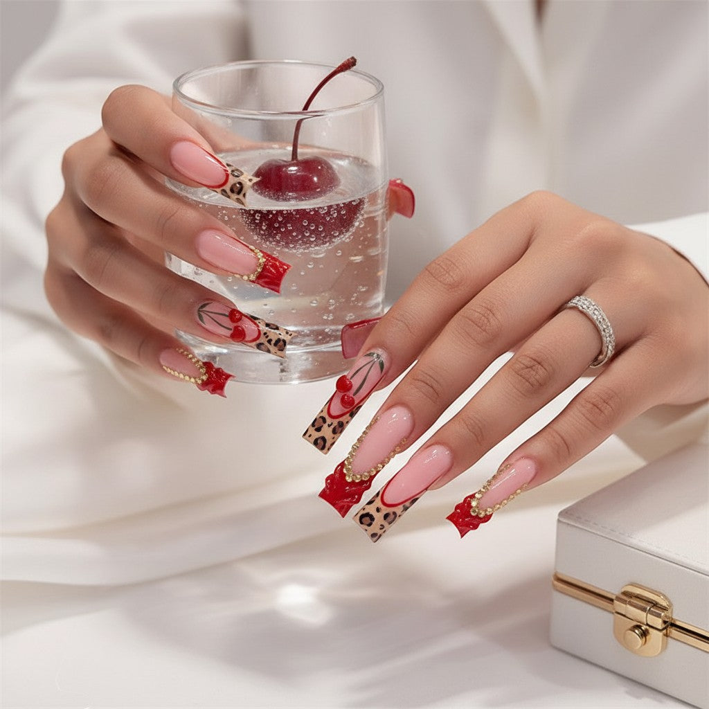AuraPress Aura62 press-on nails with pink French tips, leopard print, red cherry charms, and gold rhinestone accents.